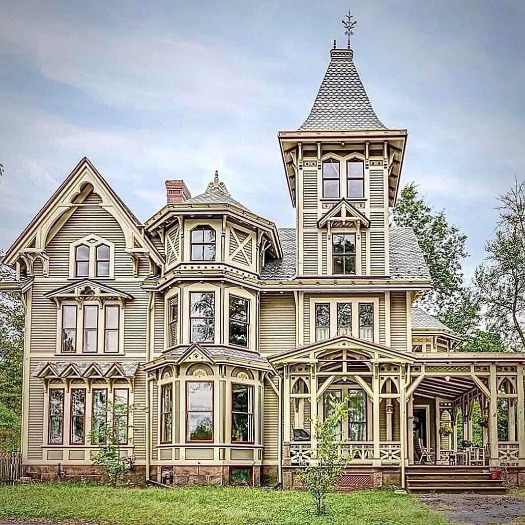 Ornate Victorian Gothic house with tall tower, decorative trim, and wraparound porch on green lawn
