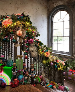 Christmas tree with tropical flowers, rainbow ornaments and beaded garlands by arched window in industrial room