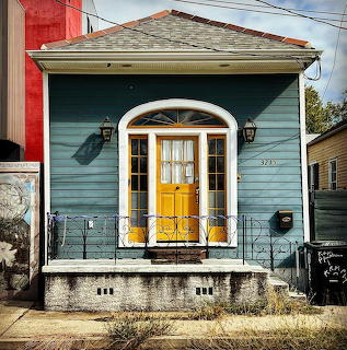 Front view of a small blue house with a yellow door and arched trim above the entrance