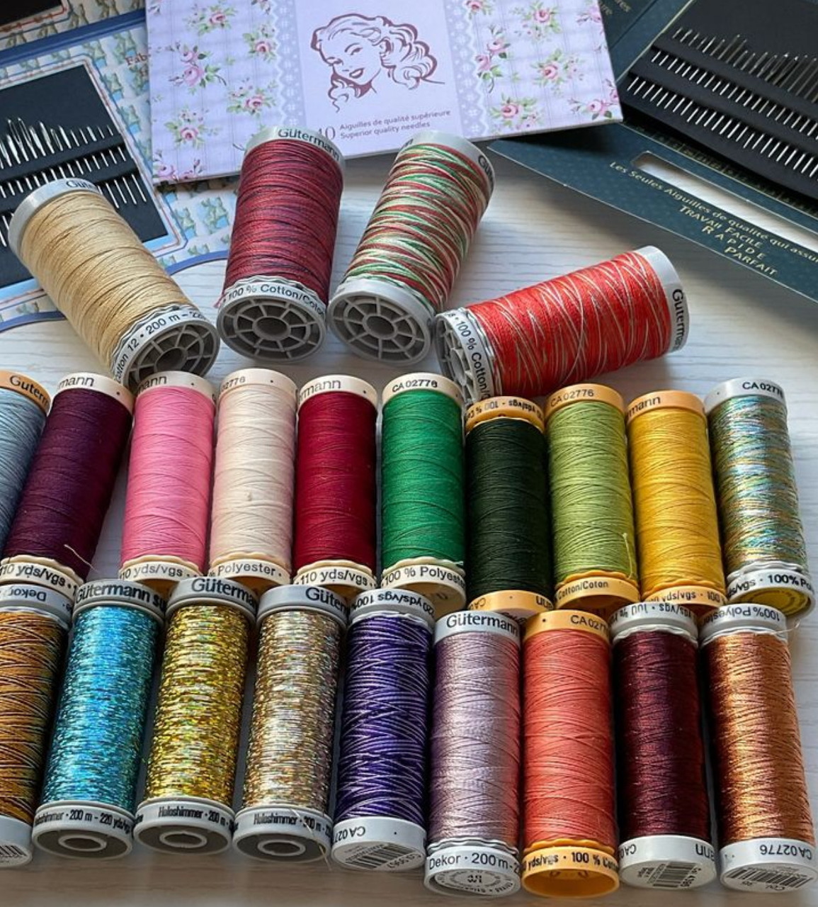 Collection of colorful sewing thread spools arranged on a white surface with sewing accessories in the background