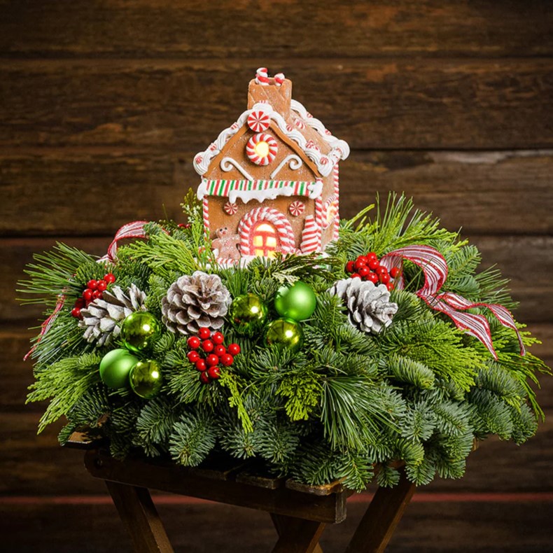 Christmas centerpiece with a gingerbread house, pinecones, berries, and green ornaments on evergreen branches