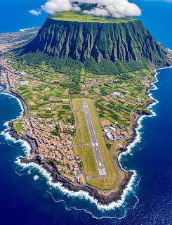 Aerial view of island airport runway with steep mountain and ocean coastline