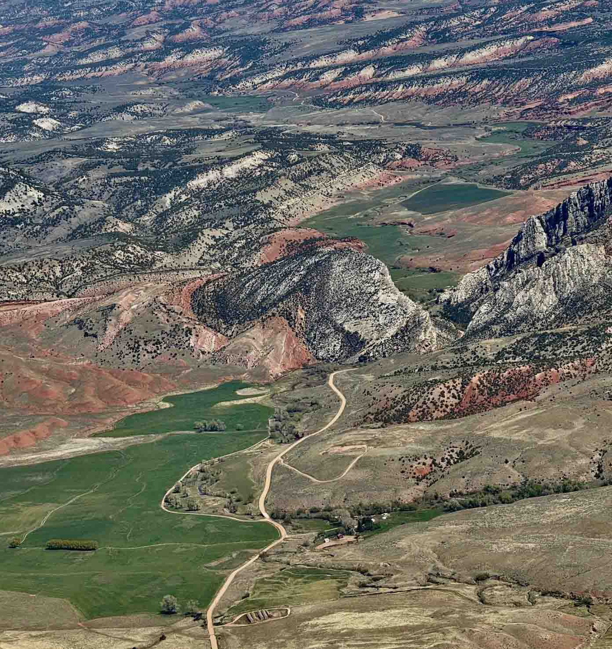 Aerial view of a winding road through a rocky valley with green fields and hills