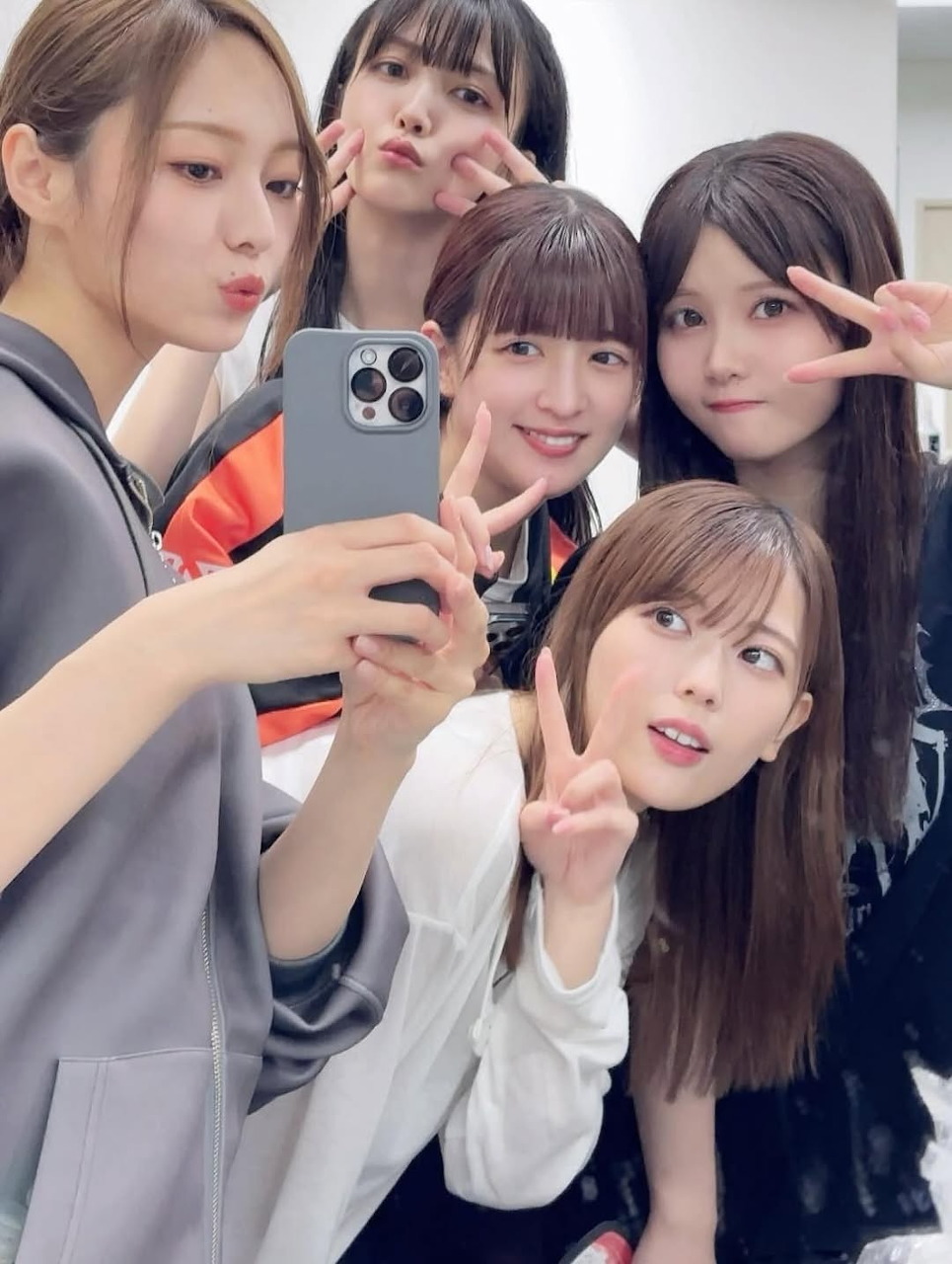 Five young women posing together for a mirror selfie, some making peace signs