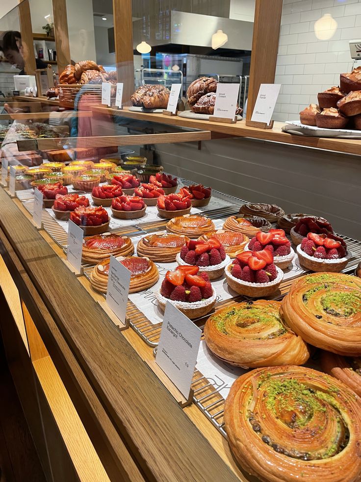 Bakery display case filled with assorted pastries, fruit tarts, and spiral danishes on wooden shelves