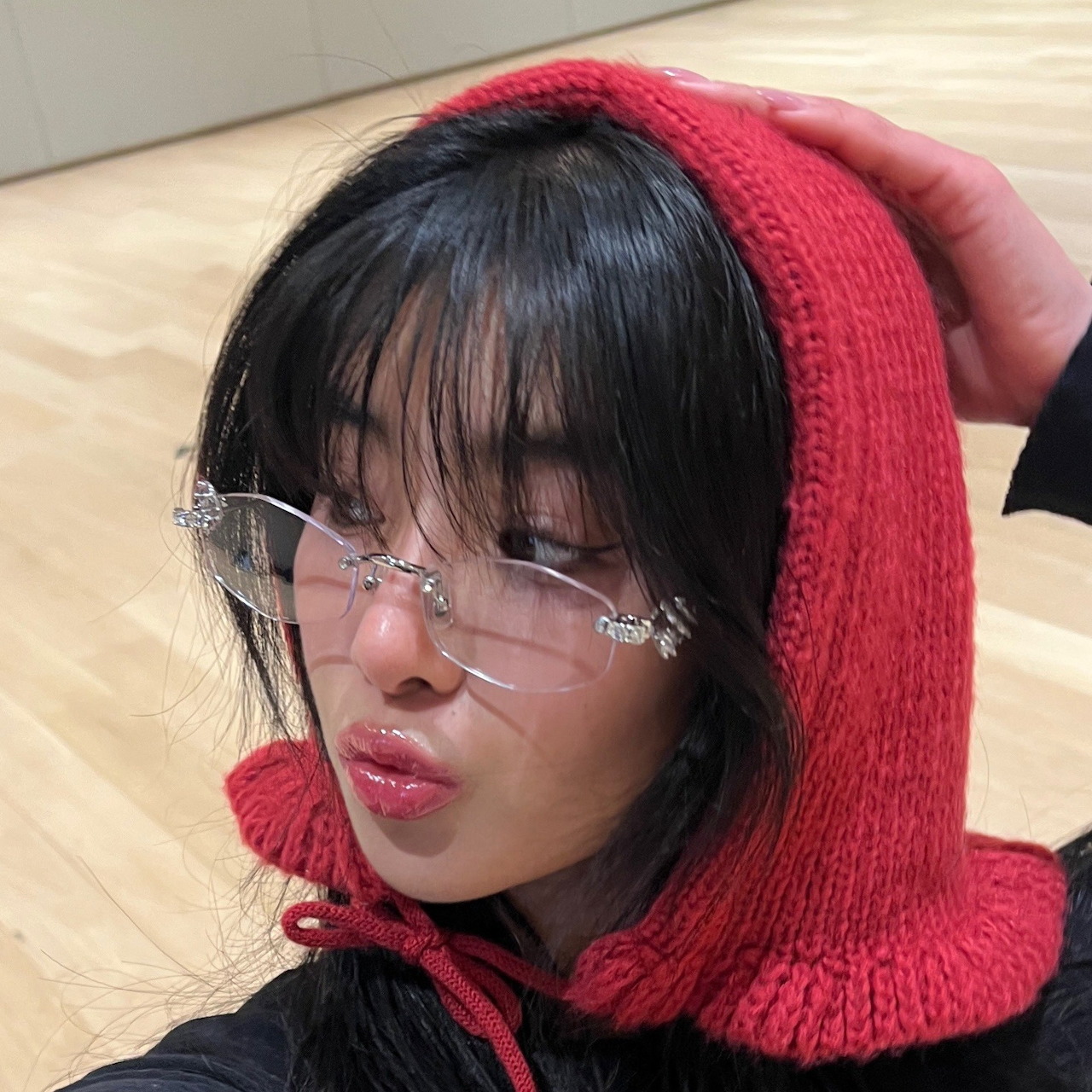 Young woman in red knit hood and clear glasses looking to the side