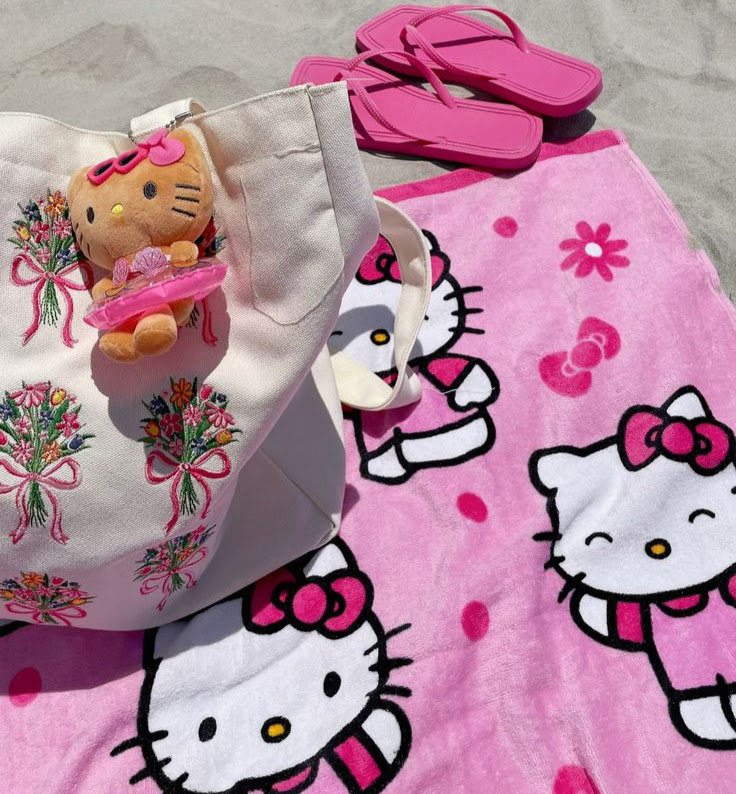 Hello Kitty pink beach towel, tote bag with floral print, plush doll, and pink flip flops on sand