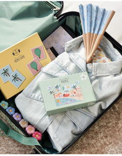 Open green suitcase with folded robe, paper fan, puzzle box, and travel accessories