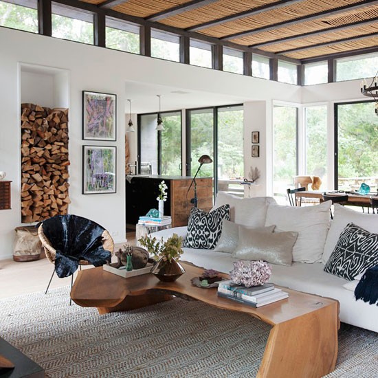 Modern living room with white couch, wood table, ceiling beams, and large windows with natural light
