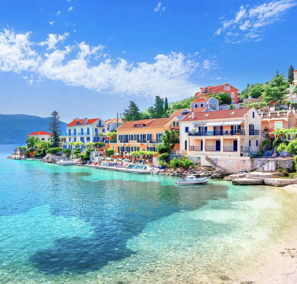 Vibrant Mediterranean village with colorful buildings along a crystal-clear turquoise waterfront and sandy beach