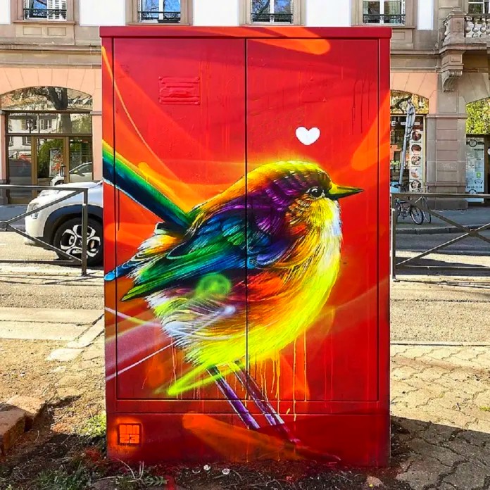 Colorful bird mural with rainbow feathers painted on red street utility box