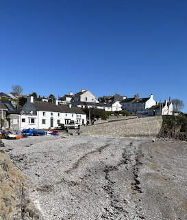 Coastal village with white houses above a pebble beach with boats and stone seawall under blue sky