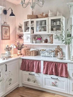 Cozy white cottage kitchen with glass cabinets, floral details, baskets, and red gingham sink curtains