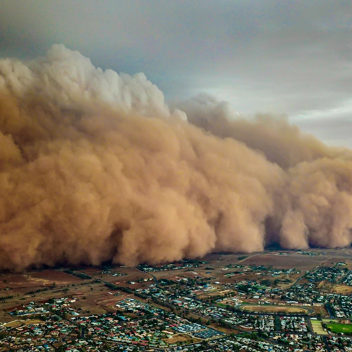 Large dust storm with orange clouds approaching city with houses and buildings