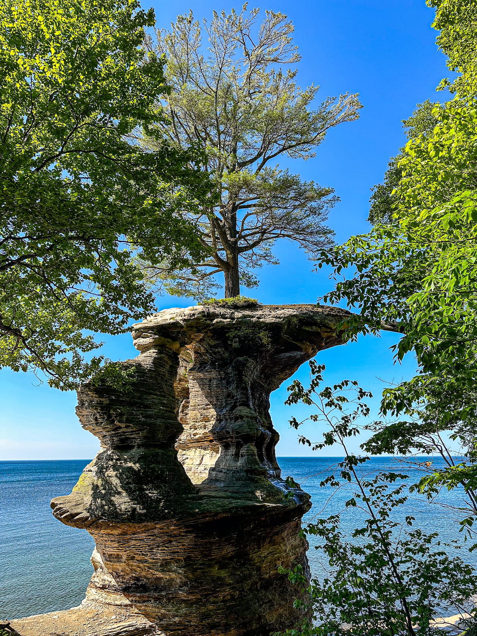 Chapel Rock formation with tree on top against blue sky and Lake Superior water