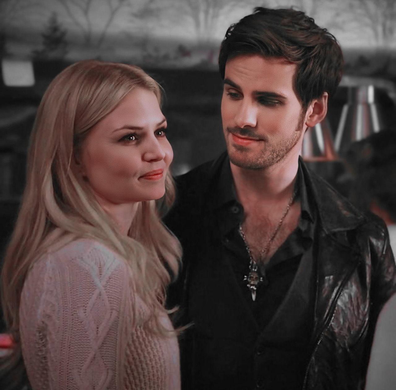 Woman in a light sweater beside a man in a black leather jacket, looking at each other indoors