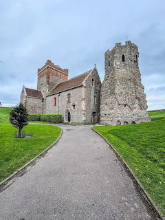 Roman Pharos ruins and medieval church at Dover Castle with paved path and green lawn under cloudy sky