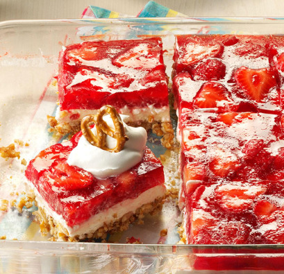 Red strawberry pretzel bars with cream cheese layer on white platter