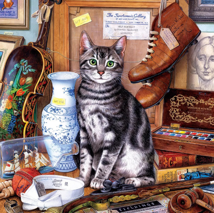 Gray tabby cat sitting on desk surrounded by antiques, violin, ship in bottle, old books and vintage collectibles