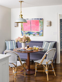 Round wood table with woven chairs and striped cushions in a bright white dining nook with abstract pink artwork