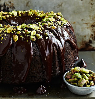 Dark chocolate bundt cake with glossy ganache and chopped pistachios, beside a small bowl of pistachios.