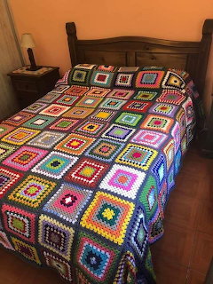 Colorful crocheted granny square blanket with rainbow patterns on wooden bed