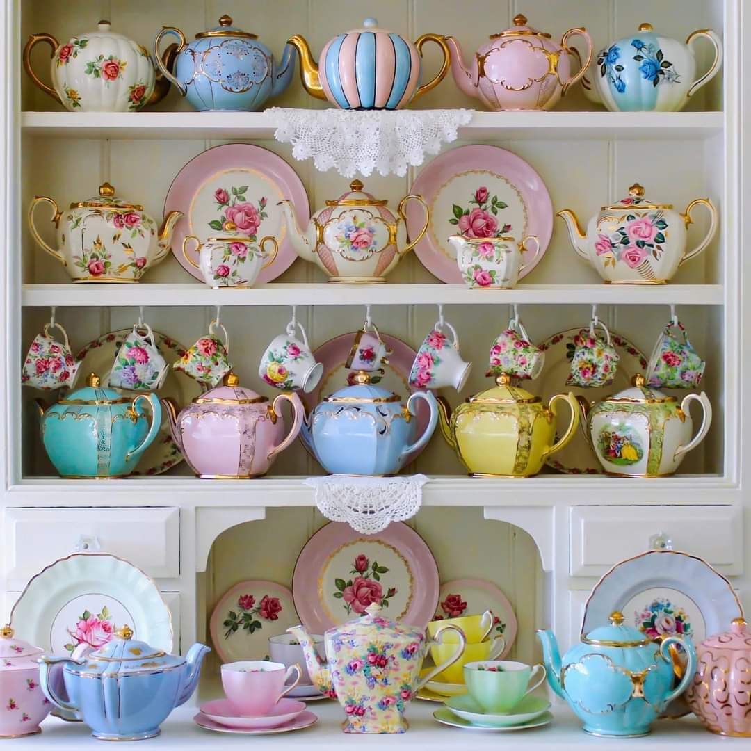 White cabinet shelves filled with colorful vintage floral teapots, plates, and teacups in pastel colors