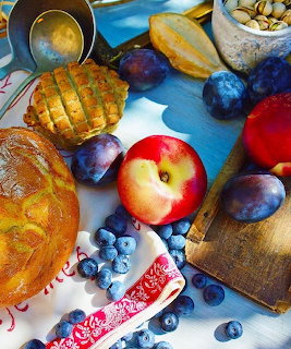 Still life of bread, pastries, plums, blueberries, nuts, and an apple on a table