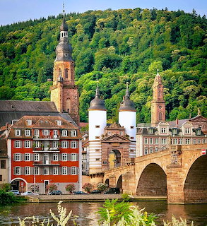 Heidelberg Old Bridge with white towers, church spires, and colorful buildings against a green hillside