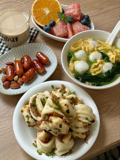 Korean dishes including sausages, soup with egg and vegetables, dumplings, strawberries, and beverage on wood table