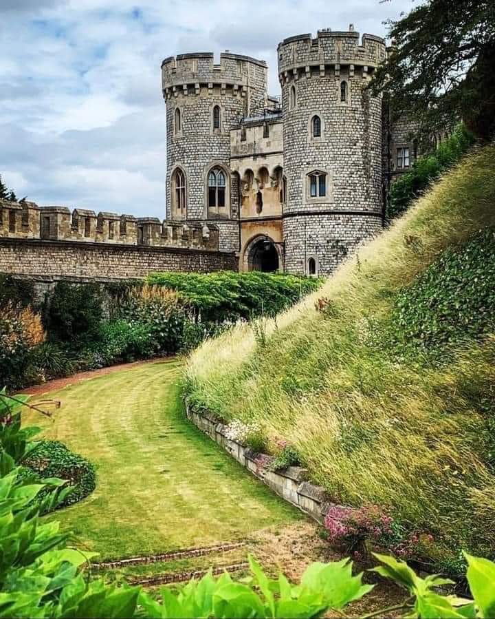 Stone castle with round towers above a grassy hillside and garden path