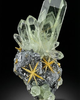 Large clear quartz crystals on dark mineral base with golden star-shaped rutile and green fluorite