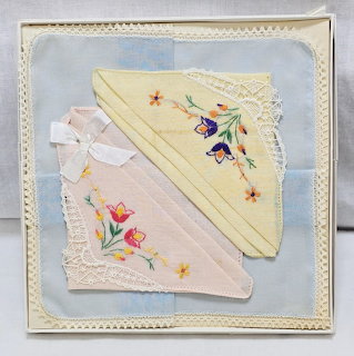 Two vintage embroidered handkerchiefs with lace edges displayed in a pale blue box