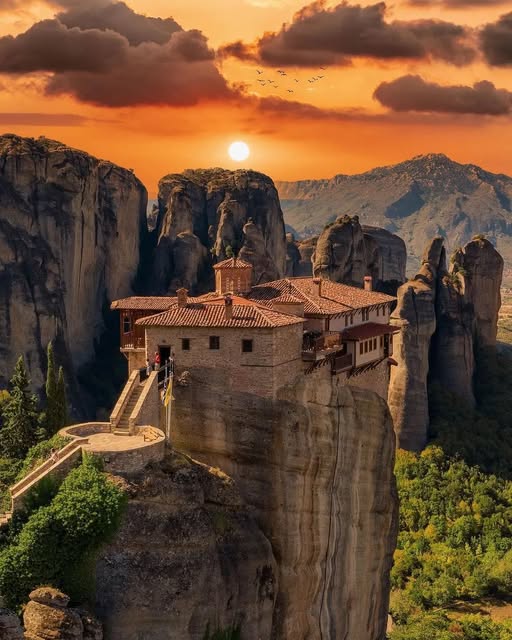Greek monastery on a cliff top in Meteora with orange sunset sky and tall rock pillars