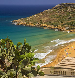 Turquoise bay and sandy beach with cactus in the foreground and a rocky hillside behind