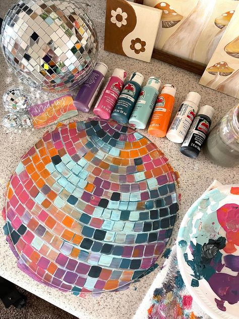 Colorful mosaic disco ball with paint bottles and craft supplies on a table