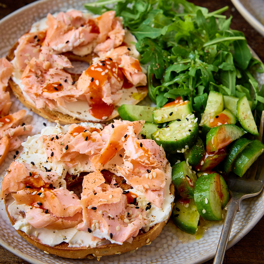Open-faced bagels with smoked salmon, cucumber salad, and leafy greens on a plate