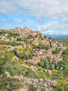 Hilltop stone village of Gordes in Provence, France, overlooking rocky green slopes under a cloudy sky.
