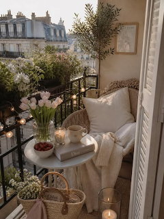 Cozy balcony with chair, small table, flowers, and city rooftops in the background