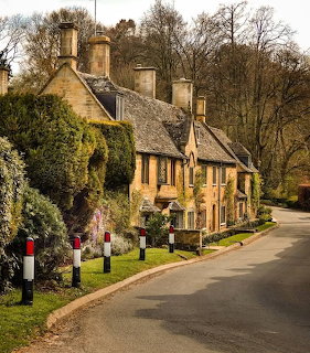 Row of historic Cotswolds stone cottages with steep roofs beside a country road in winter