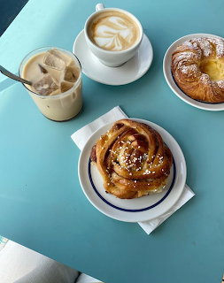 Cinnamon bun, iced latte, cappuccino, and custard pastry on a teal table