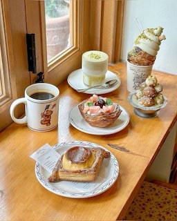 Coffee, latte, pastries, and desserts arranged on a wooden table by a window