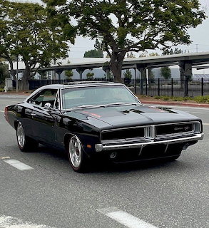 Black classic Dodge Charger R/T muscle car parked on a street with trees in the background