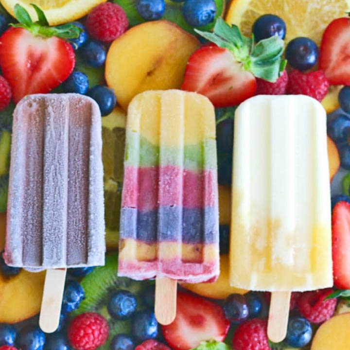 Three fruit popsicles on sticks laying on mixed fresh berries and fruit slices