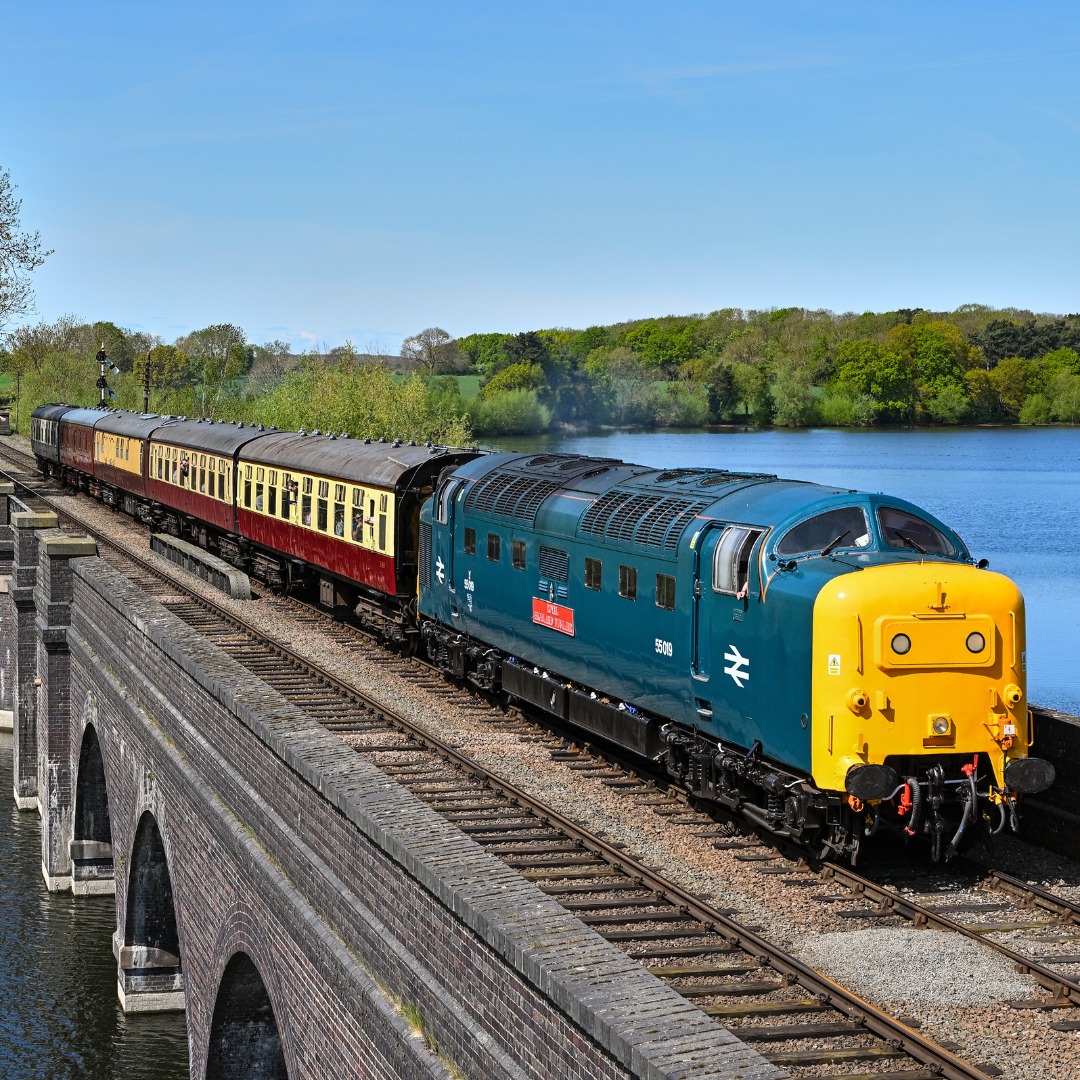 Blue vintage diesel train crossing viaduct over water with green landscape background