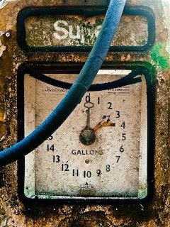 Weathered vintage gas pump gauge with rust and peeling paint, blue fuel hose across frame