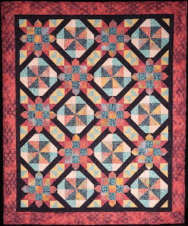 Patchwork quilt with rosette star pattern in coral, teal, and cream on pink floral border