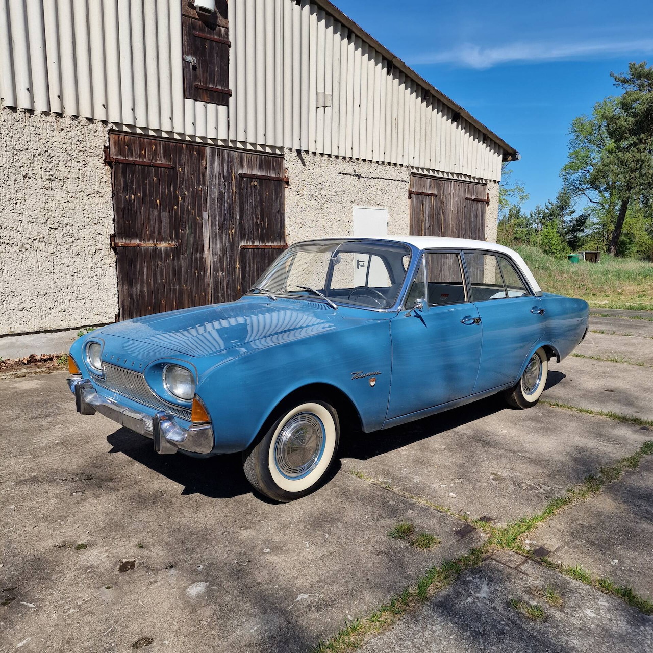 Vintage blue car with white roof parked by old barn