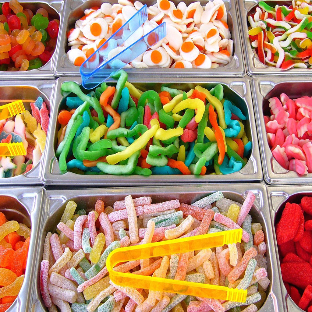 Metal trays filled with various colorful candies including gummy worms, marshmallows, and assorted sweets