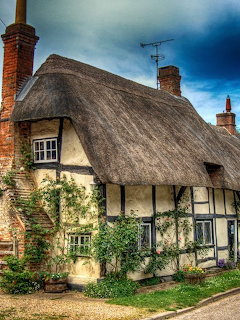 Historic thatched roof cottage with cream walls and timber framing in English village